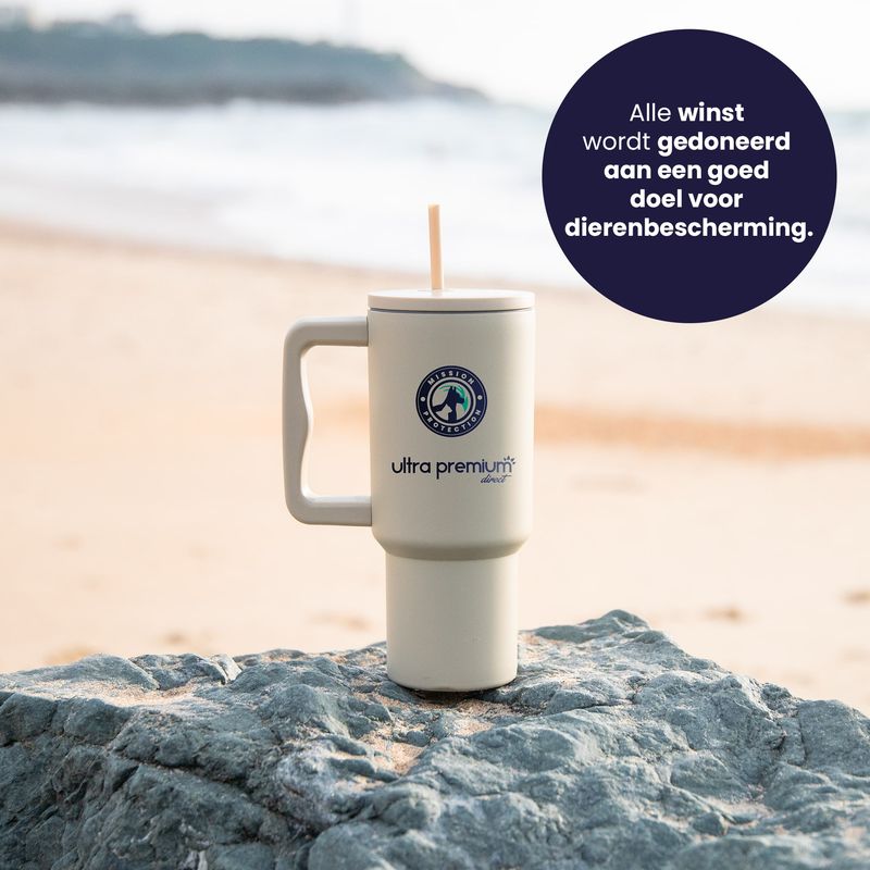 Herbruikbare mok met rietje Missie bescherming Baskenland op een rots met een strand op de achtergrond met een sticker die aangeeft dat een deel van de winst wordt gedoneerd aan een dierenbeschermingsorganisatie.